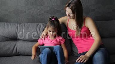 有孩子的女人用平板电脑坐在沙发上。 母亲带着孩子坐在沙发上用平板电脑